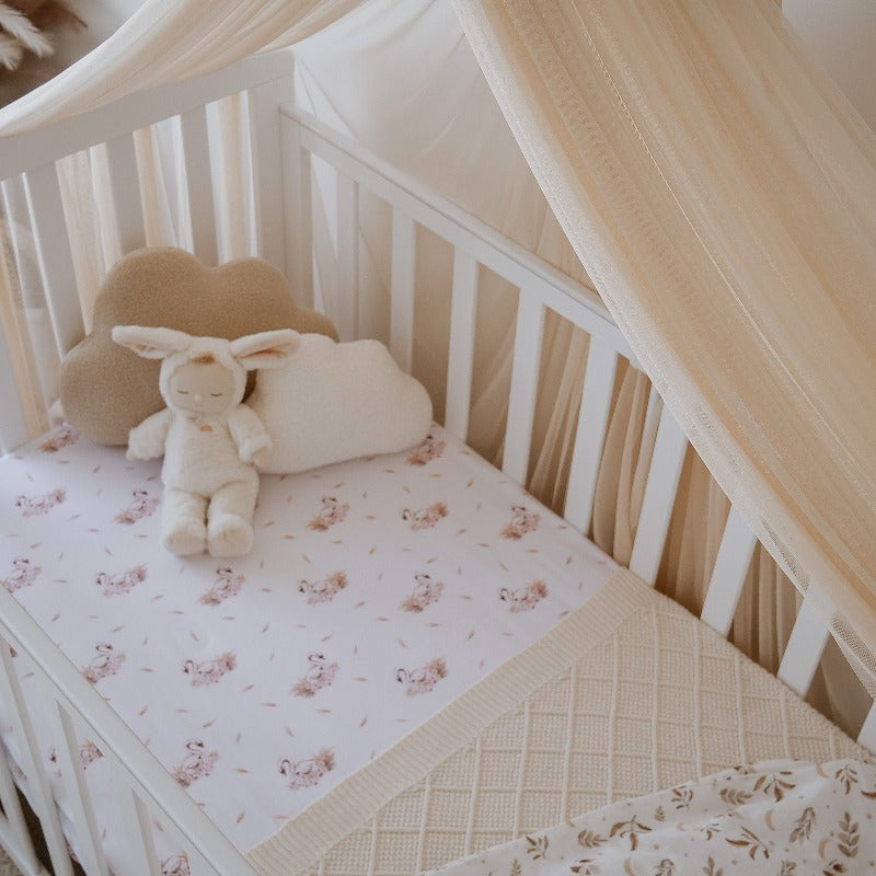 White pine crib set with swan printed linen, a cream knitted blanket and several plush toys in the top corner