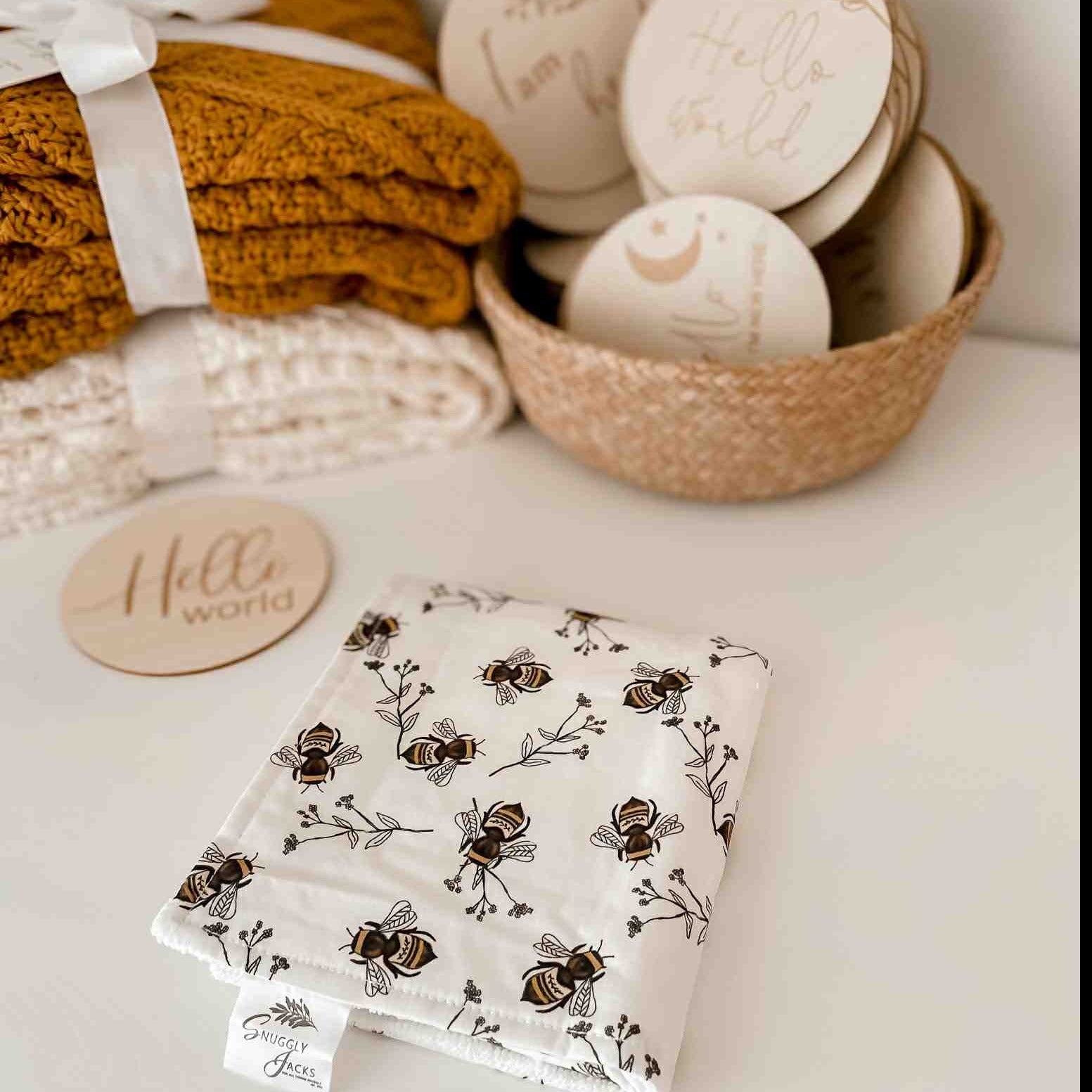 Honey and Cream Knitted Blankets beside a Burp cloth with bees yellow print placed next to an announcement disk located in Canada
