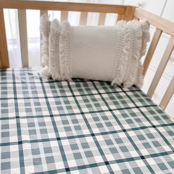 Close up of a tasseled pillow resting on top of a blue plaid fitted crib sheet
