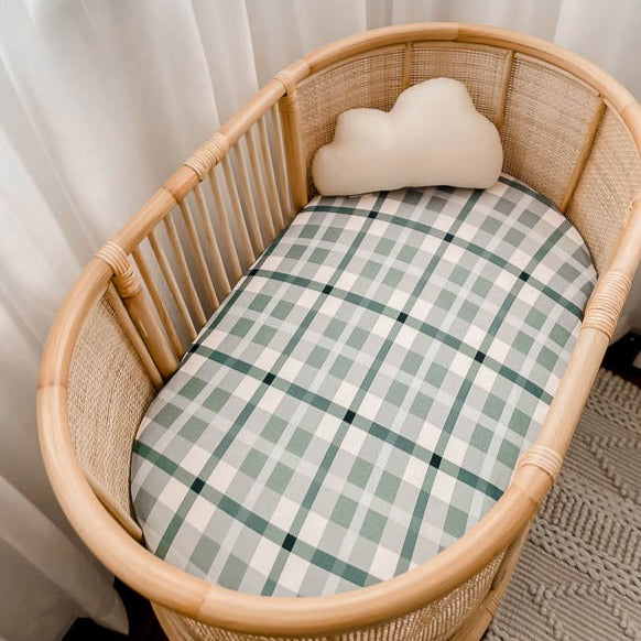 Rattan bassinet made up with a blue plaid cotton sheet and a cute little cloud pillow in the far end