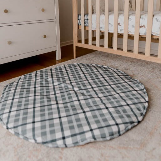 A cotton playmat on the floor of a nursery with a pine cot and a white chest of draws in the background