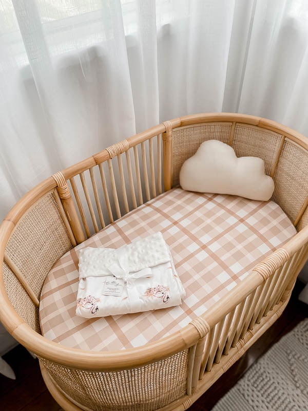 Earthy plaid bassinet sheet set in a brown cane bassinet with a cloud pillow on one side and a dimple dot minky folded up on the base of the mattress