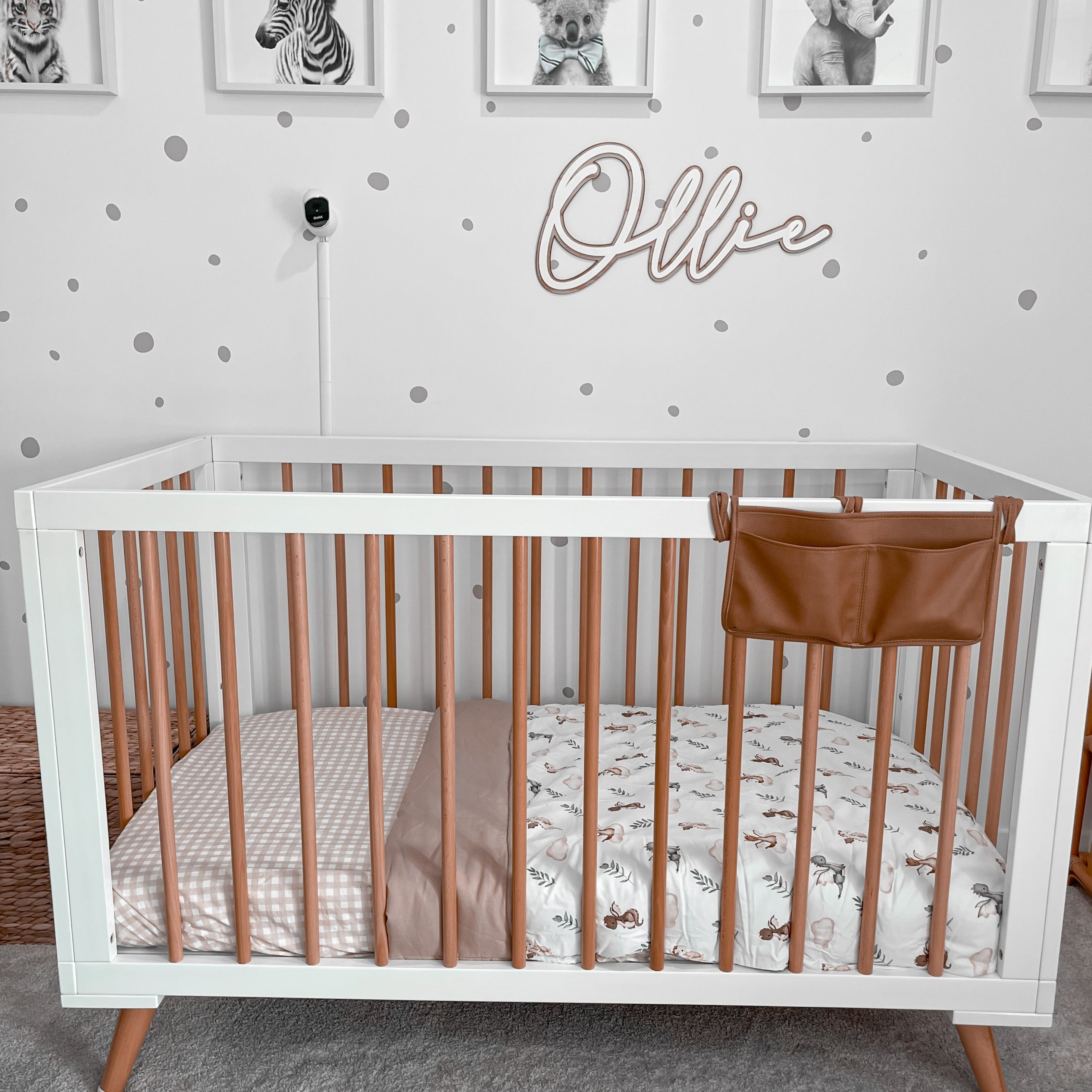 Pine crib with white accents set out in a nursery with Ollie written on the wall and cotton linen on the mattress.