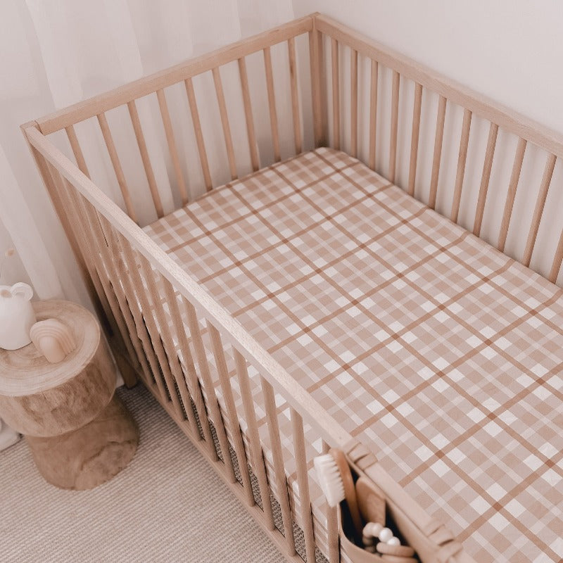 Modern nursery set including a pine crib, a bed side table made from wood and a soft brown plaid fitted sheet