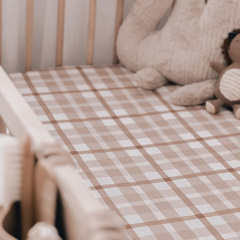 Close up of a crib made up using a brown plaid cotton sheet with a stuffed dinosaur and lion in the far right corner.