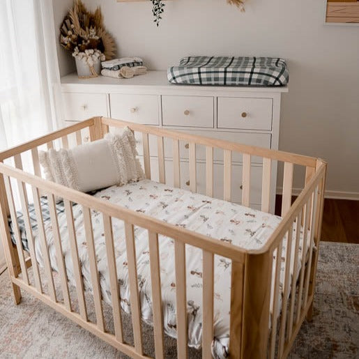 A natural pine crib set out in a modern nursery made up using blue plaid cot sheet and a crib quilt with dragon prints.