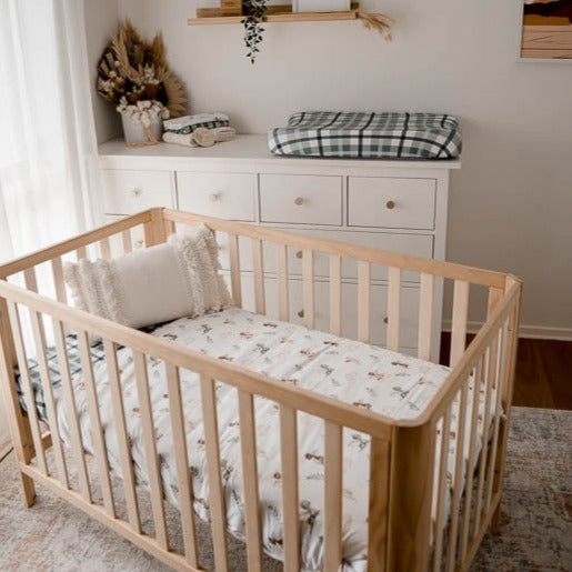 A natural pine crib set out in a modern nursery made up using blue plaid cot sheet and a crib quilt with dragon prints.