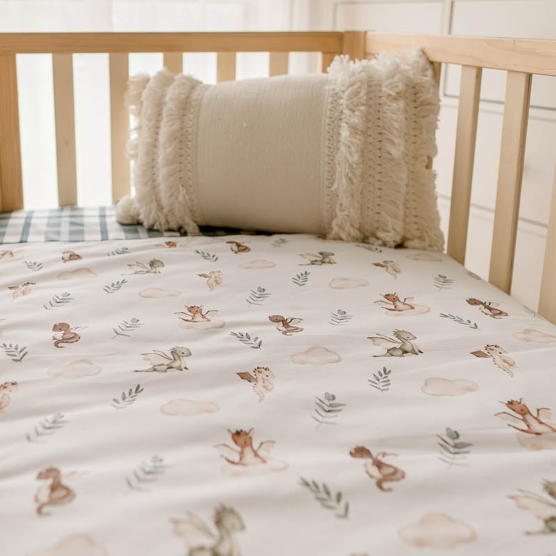 A low angel shot of a crib quilt with dragon prints and a tasselled pillow in the background