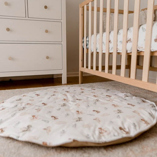 Image of a play mat with a white base and cute dragons spread out all over it set in the middle of a nursery with a white chest of draws and a pine crib