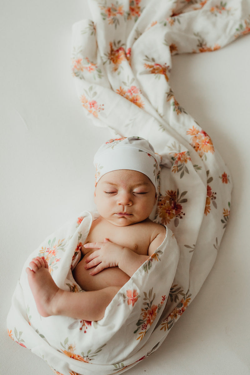 Muslin Wrap with a pink floral draped over a table snuggly wrapped a baby at one end. 