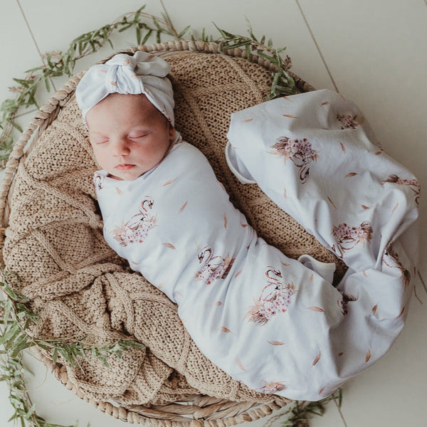 Sweet little baby snuggled in to a taupe knitted blanket and wrapped in a swan printed jersey stretch wrap 