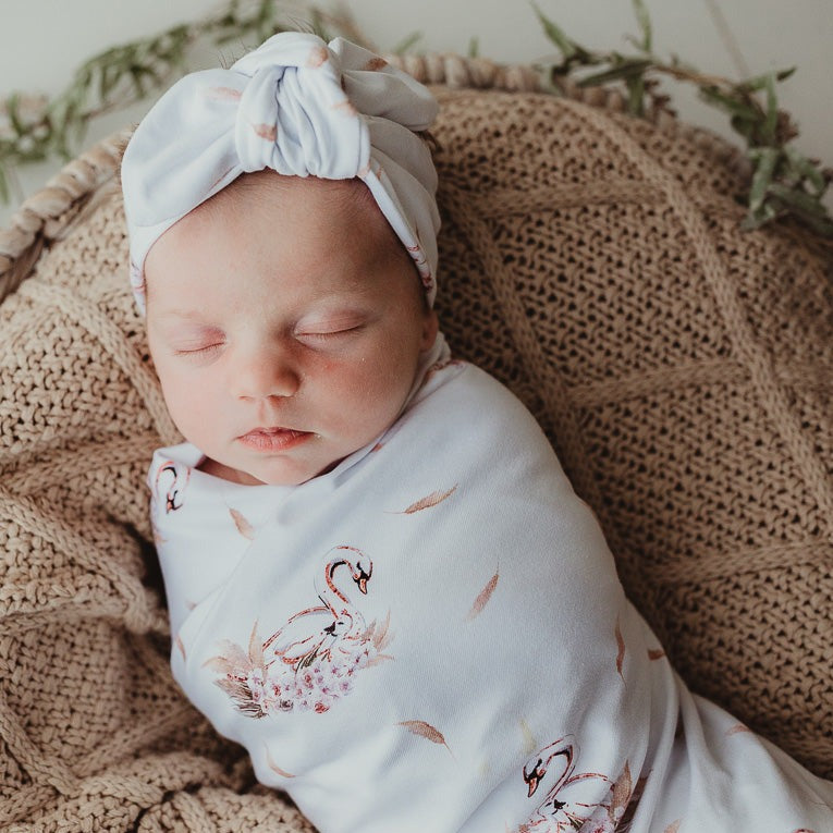 Baby sleeping while snug in a jersey stretch swaddle wrap and laying on a cotton knitted blanket.