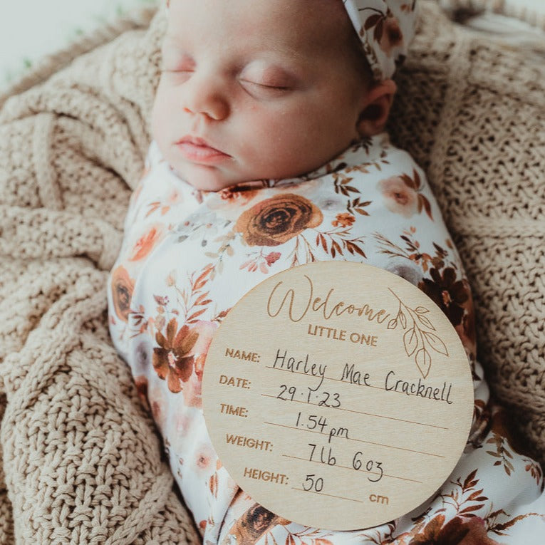 Snuggly swaddled baby with an announcement disc sleeping on top of a cotton blanket