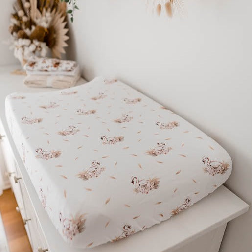 White change pad cover with soft pink swans placed in a seamless pattern set out on a whit pine change table.