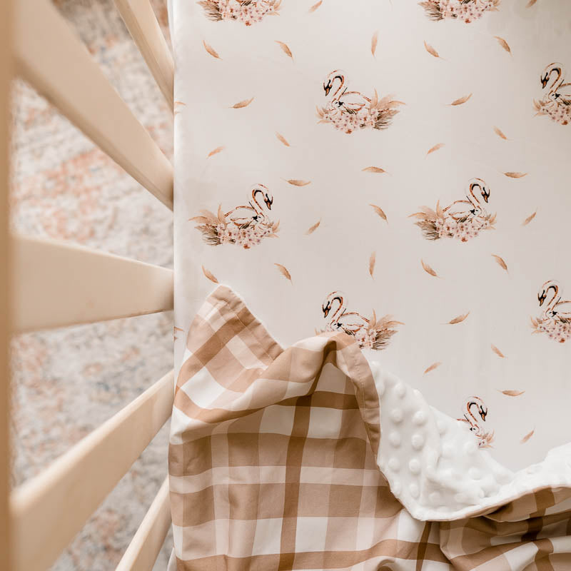 Elegant swan print on a 100% cotton sheet depicted in a pine crib, there is a soft brown dimple dot minky draped over the sheet.