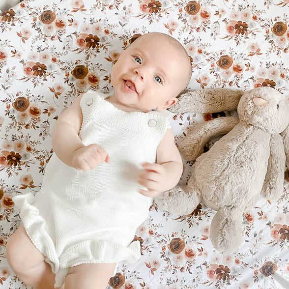 Sweet blue eyed baby laying beside a stuffed bunny on a fitted crib sheet