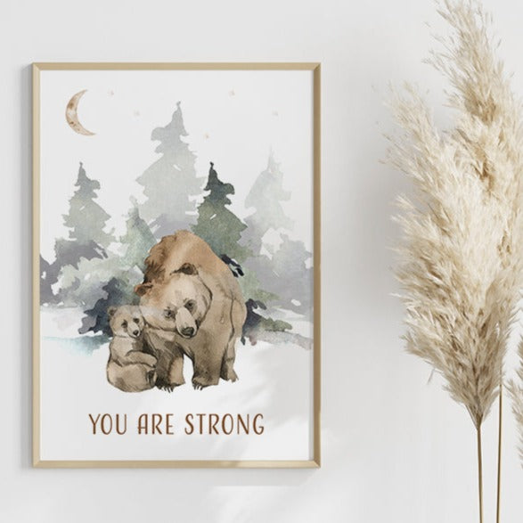 Wooden framed picture of a bear and its cub in the forest hanging on a wall with padanus grass next to it.